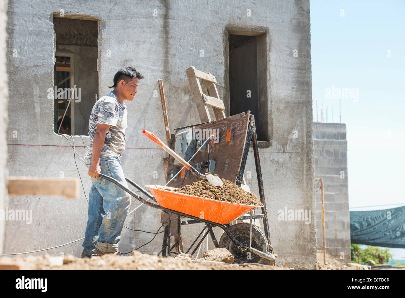 Hispanic construction worker pushing wheelbarrow at construction site Banque D'Images