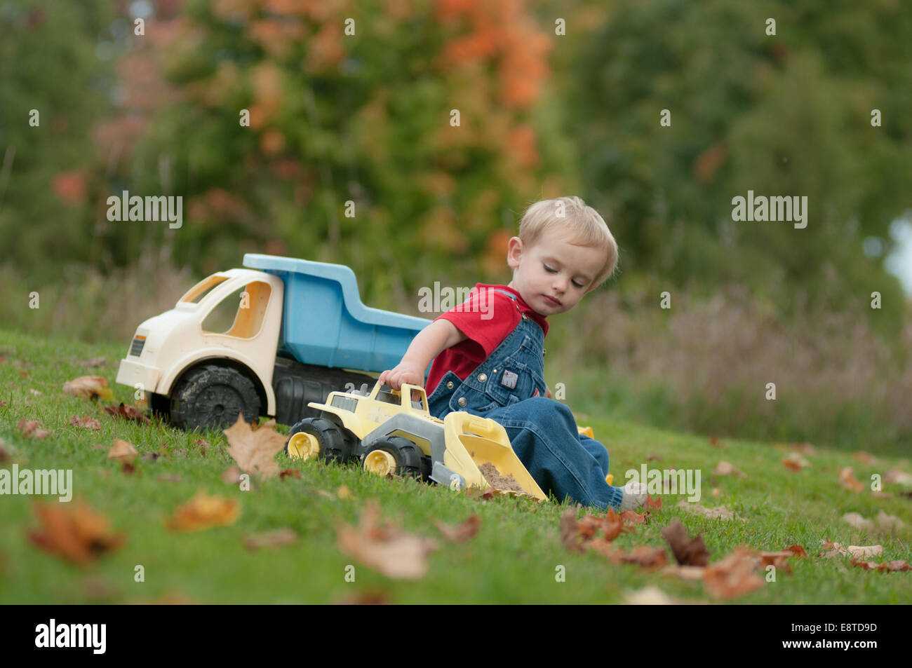 Un deux-année-vieux garçon joue avec des camions de jouets sur une journée d'automne. Banque D'Images