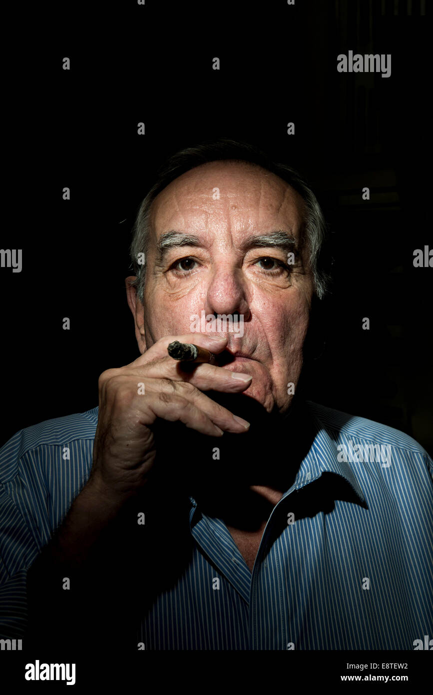 Un vieil homme blanc avec un visage de caractère, lumières et fume un cigare sur un fond noir, avec une photo de l'atmosphère sombre et Banque D'Images