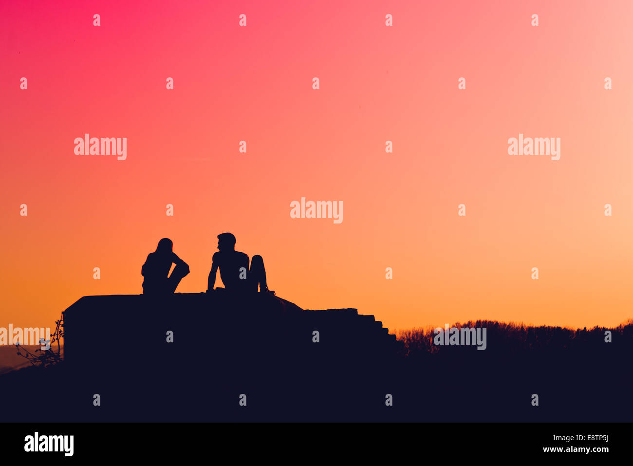 Silhouettes de young love couple sitting outdoors et parler à l'automne coucher du soleil Banque D'Images