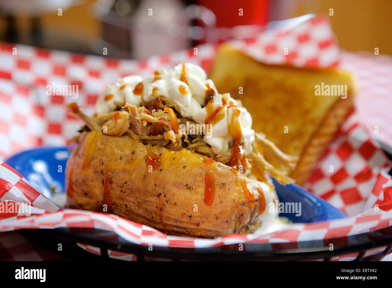 Pomme de terre au four farcies avec un barbecue de porc et surmonté de crème sure et de sauce chaude. Banque D'Images