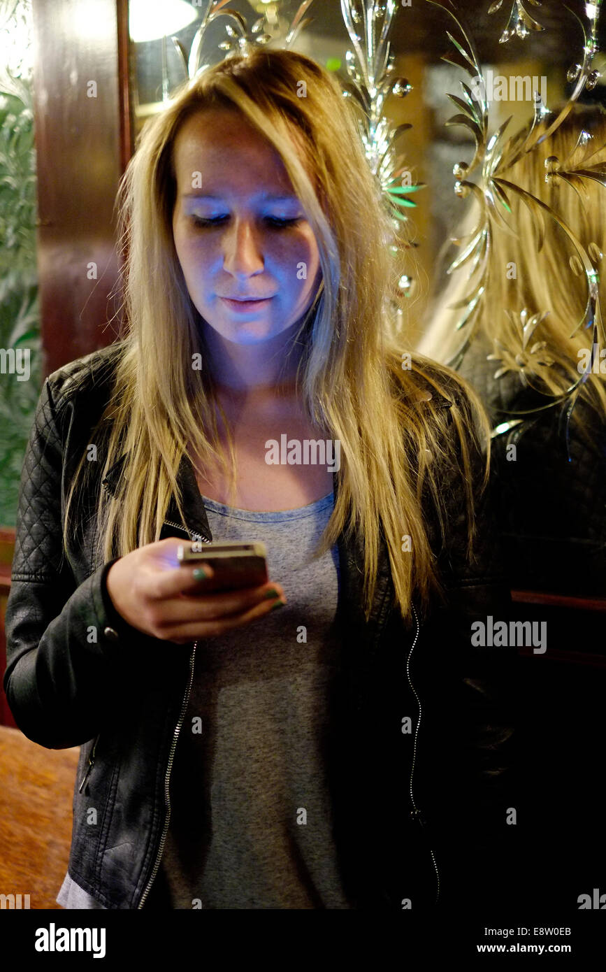 Jeune femme contrôler son téléphone intelligent tout en maintenant une bière dans un pub anglais traditionnel l'Eldon arms uk angleterre southsea Banque D'Images