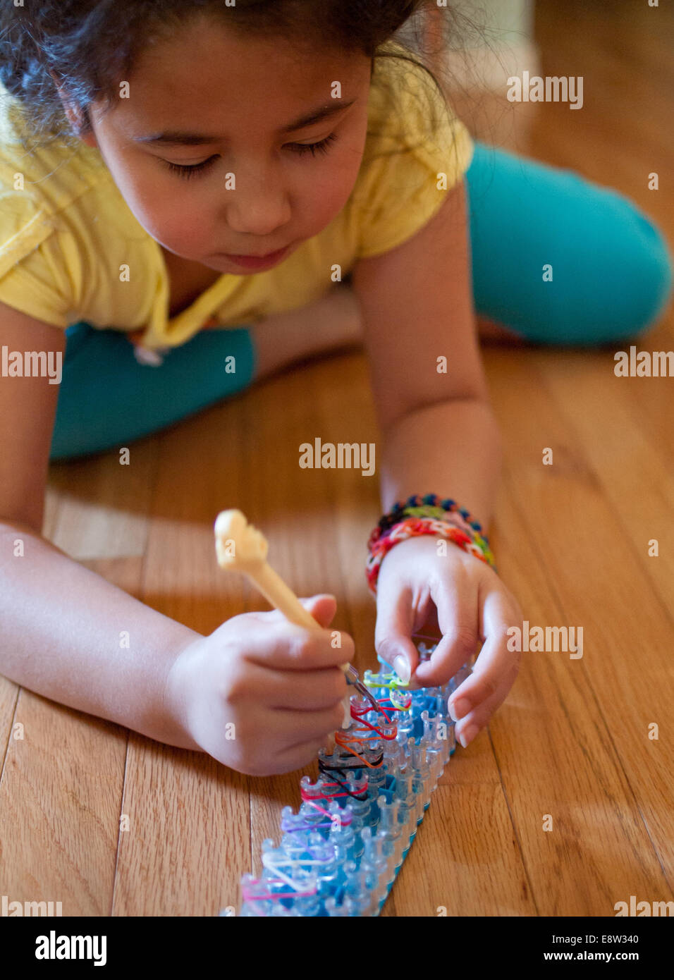 Une mignonne petite fille tisse un bracelet à l'aide d'un arc-en-ciel, un  jouet populaire utilisé pour tisser des bandes de caoutchouc en bracelets  et charms Photo Stock - Alamy