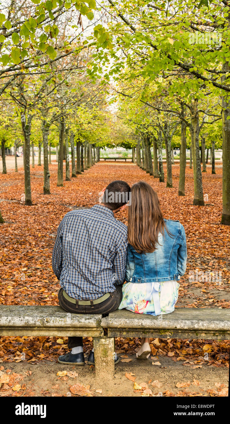 Vue arrière d'un jeune couple assis tête en tête sur un banc dans un parc urbain à l'automne Banque D'Images