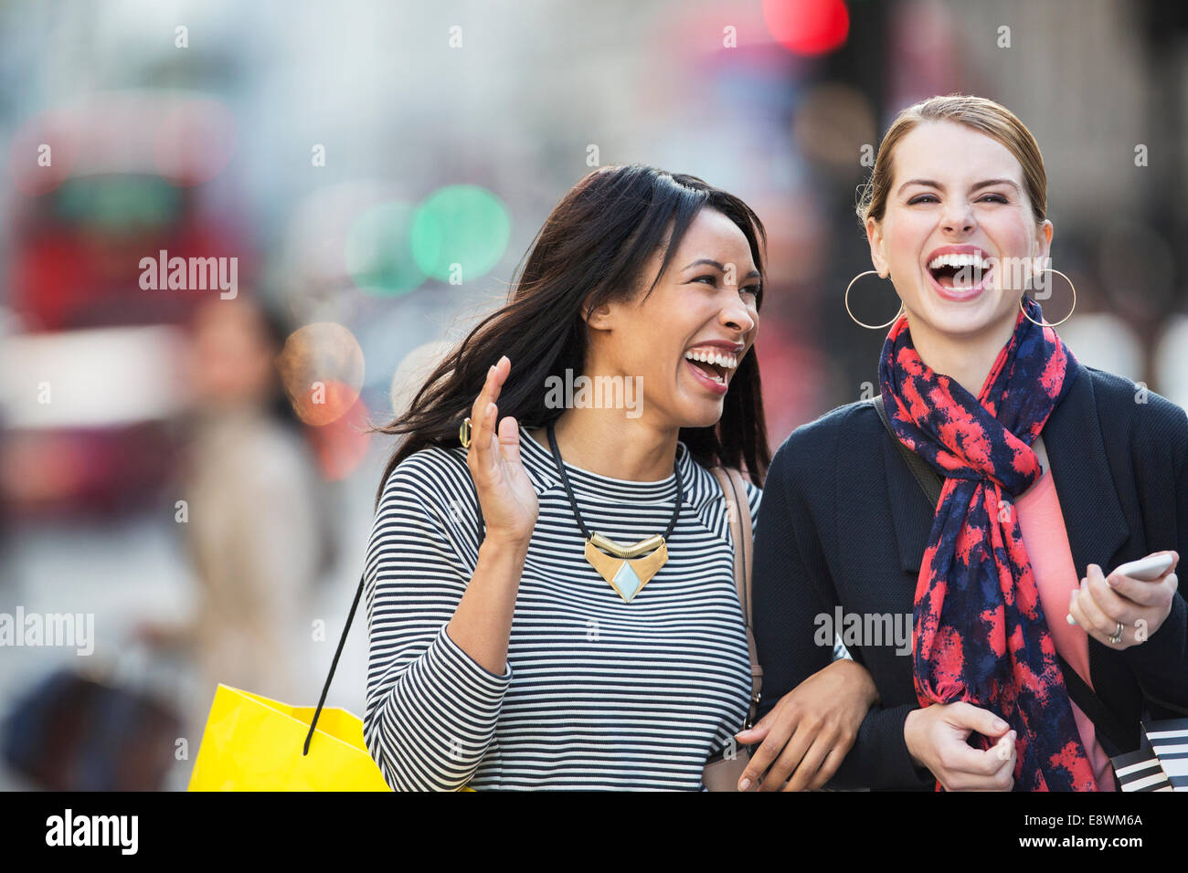 Les femmes rient ensemble walking down city street Banque D'Images