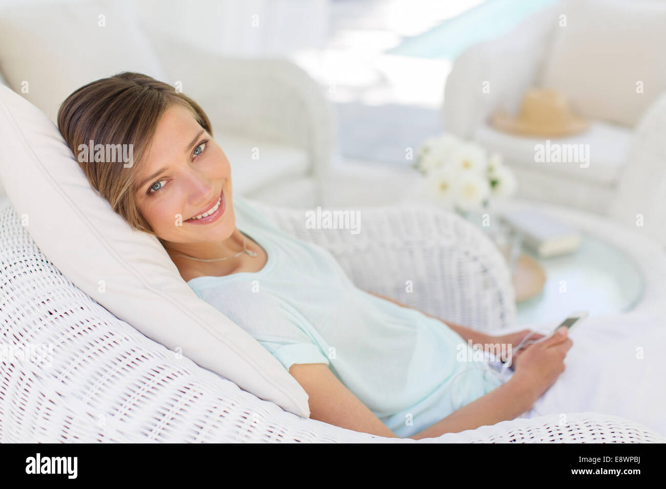 Smiling woman using cell phone in wicker chair Banque D'Images