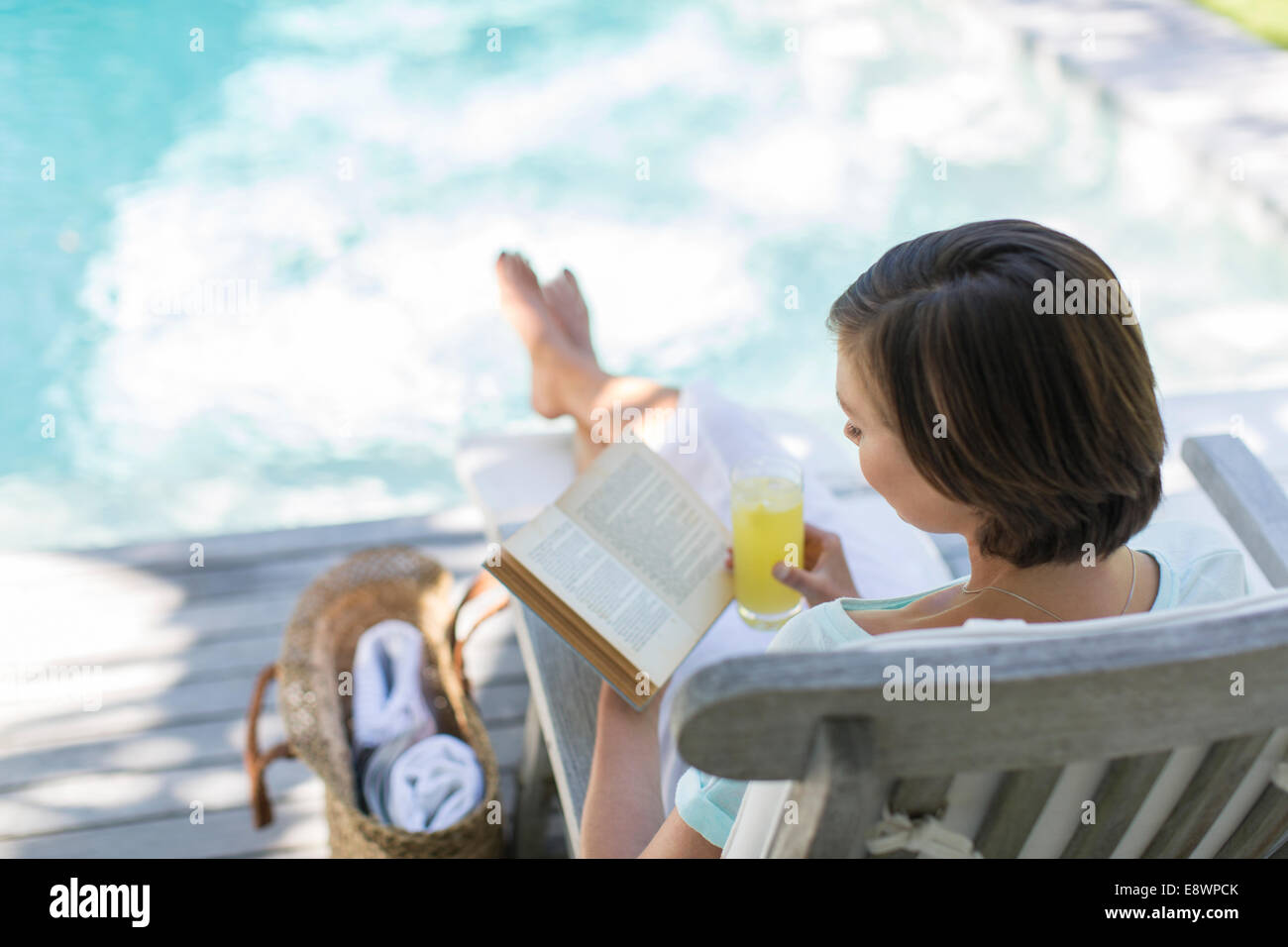 Portrait de femme lisant et boire du jus par piscine Banque D'Images