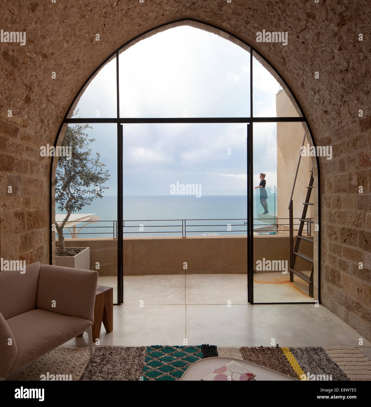 Vue à travers la fenêtre arquée à femme debout sur un balcon avec vue sur mer Chambre bâtiment T, Israël, Moyen Orient. Banque D'Images