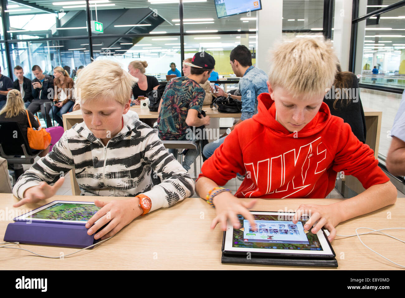 Des garçons jouent à des jeux sur leurs tablettes, l'aéroport de Schiphol, Pays-Bas Banque D'Images