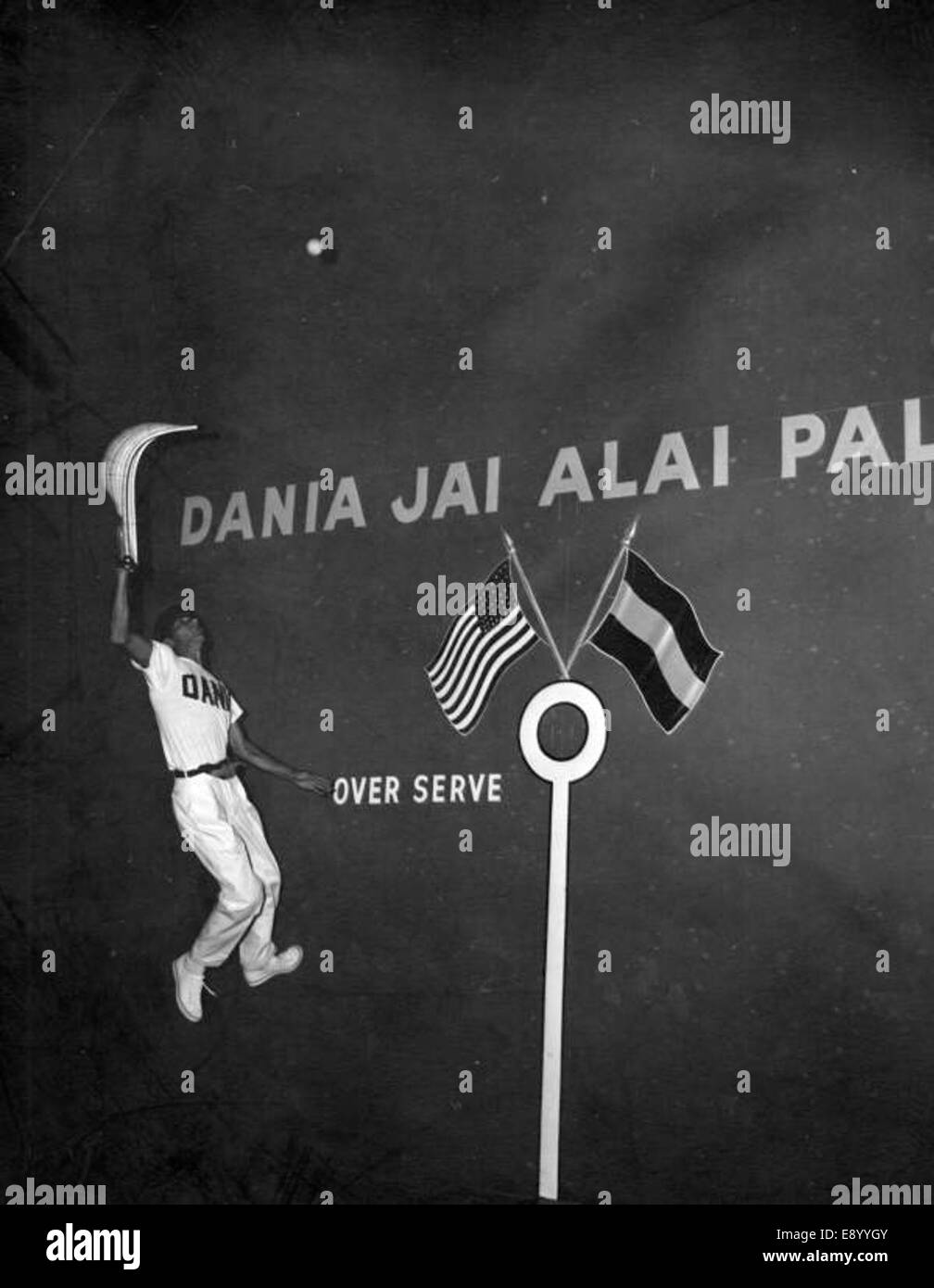 Un joueur de Jai-alai est capturé en plein air, sautant sur le fronton lors d'un match à Dania, en Floride. L'image met en évidence l'athlétisme et l'habileté impliqués dans le sport de Jai alai, avec le joueur en action. Banque D'Images