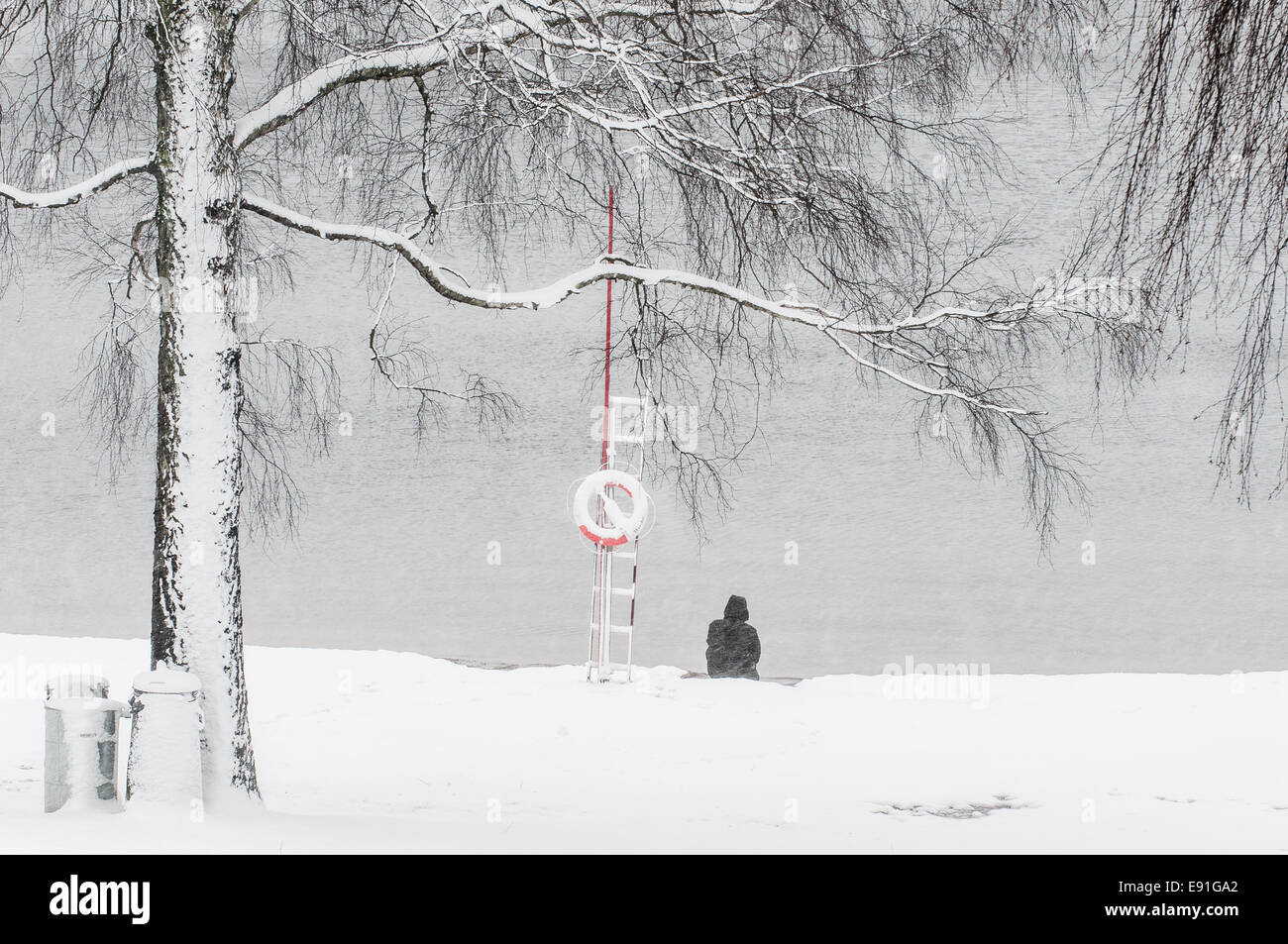 Un homme est assis au bord d'un lac en hiver Banque D'Images