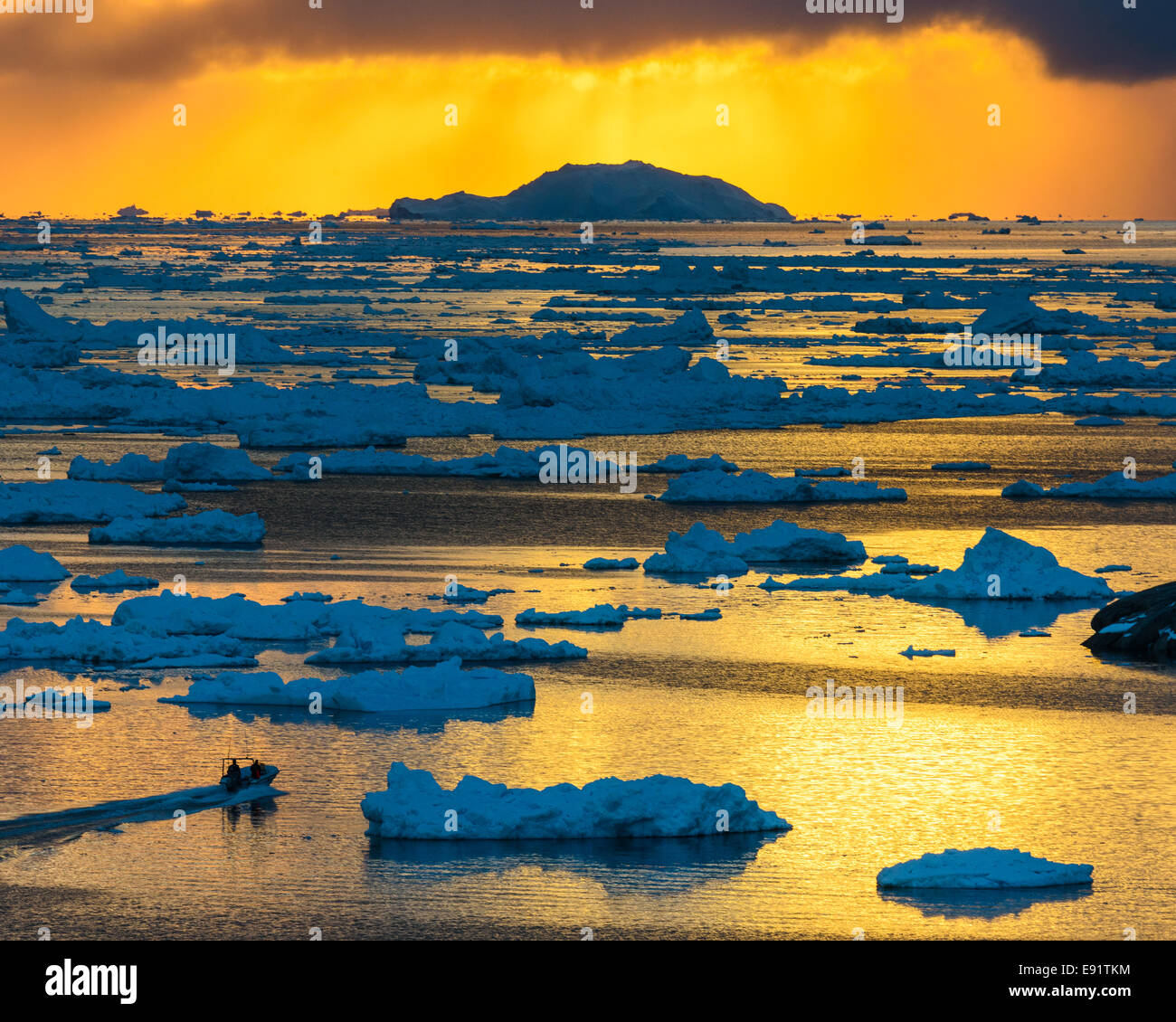 Deux personnes un bateau de direction par les eaux du glacier-remplie au coucher du soleil. Ilulissat, Groenland. Banque D'Images