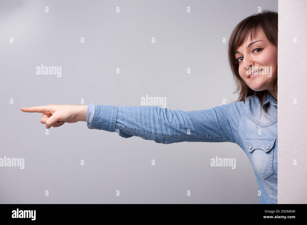 Girl pointing out avec son bras entier derrière le mur Banque D'Images