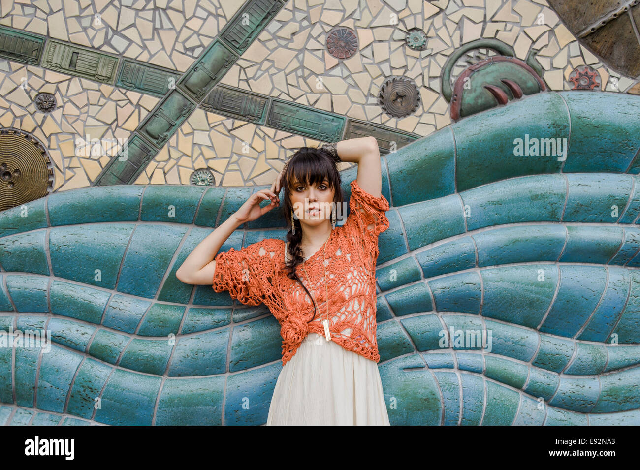 Jeune femme en Pull Crochet Orange contre mur mosaïque bleu Banque D'Images
