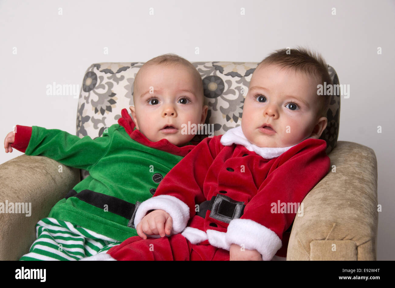 Frère jumeau un bébé de 9 mois les garçons portant un costume père noël et un elfe sur leur premier Noël, les deux assis sur une chaise Banque D'Images
