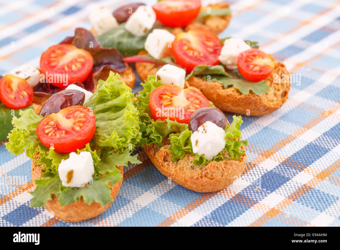Des sandwichs avec des biscottes, légumes, olives et fromage feta sur nappe colorée. Banque D'Images
