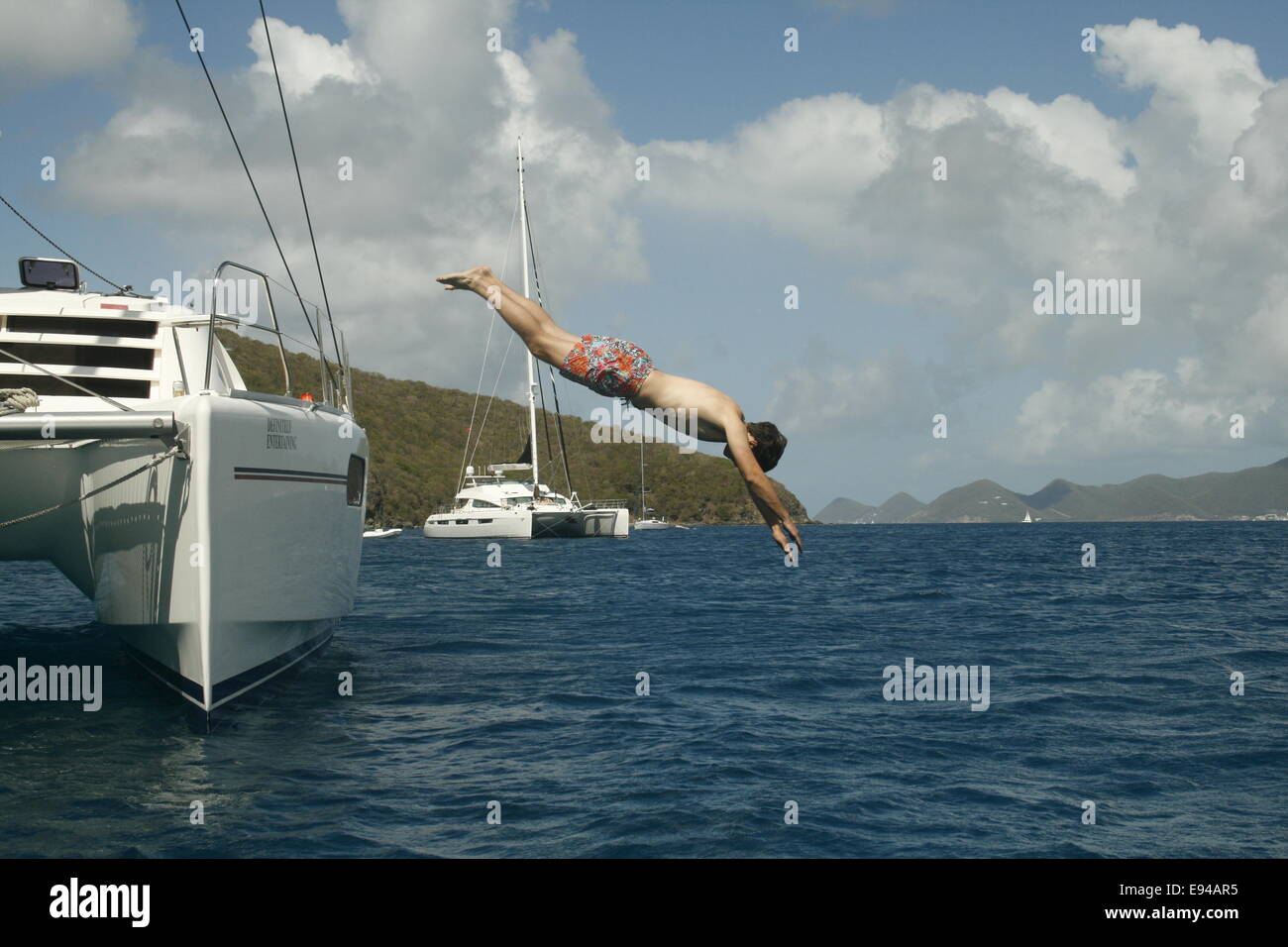 Jeune homme plonge vers le côté d'un grand catamaran à dans les magnifiques eaux bleues de la Caraïbes. Banque D'Images
