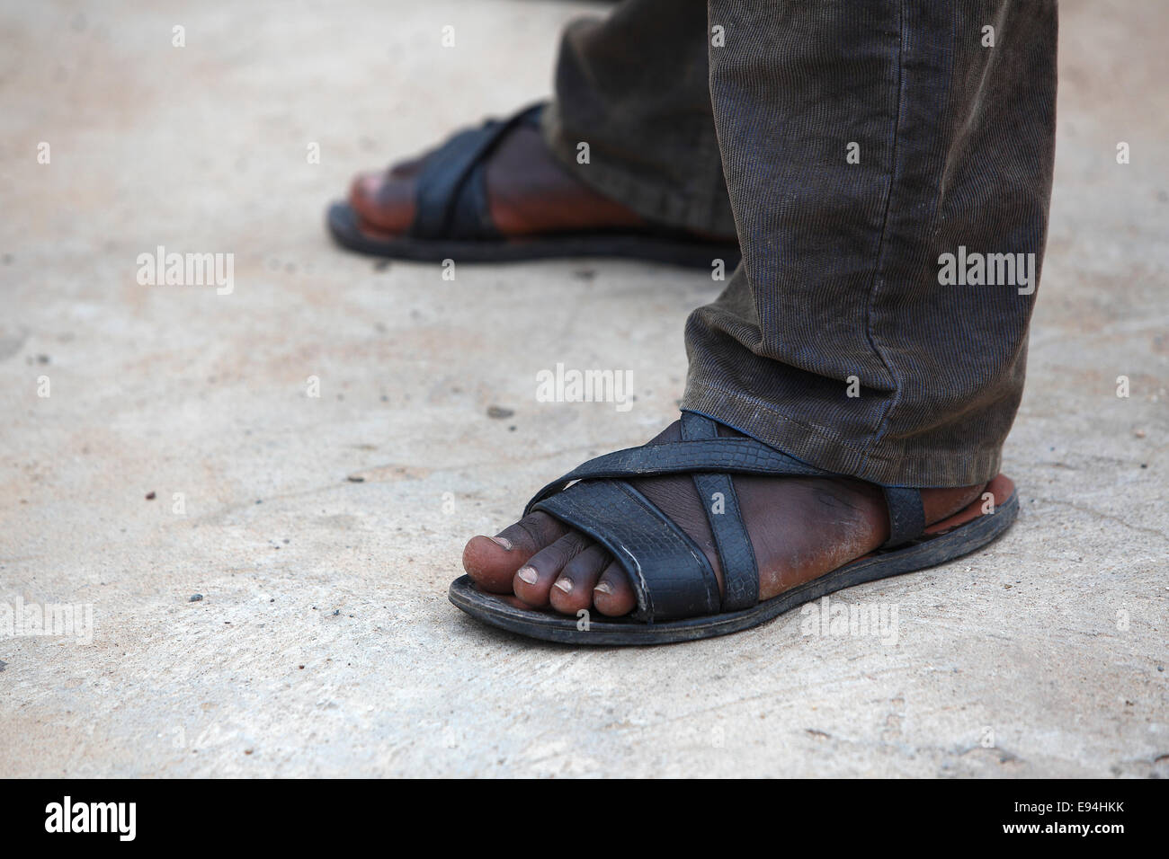 Pieds d'un homme africain avec de longs pantalons marron Banque D'Images