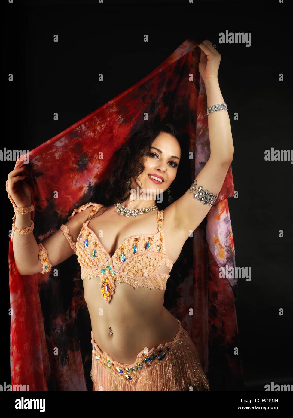 Jeune belle danseuse du ventre portant un costume coloré et un voile rouge, en face de l'arrière-plan noir. Banque D'Images