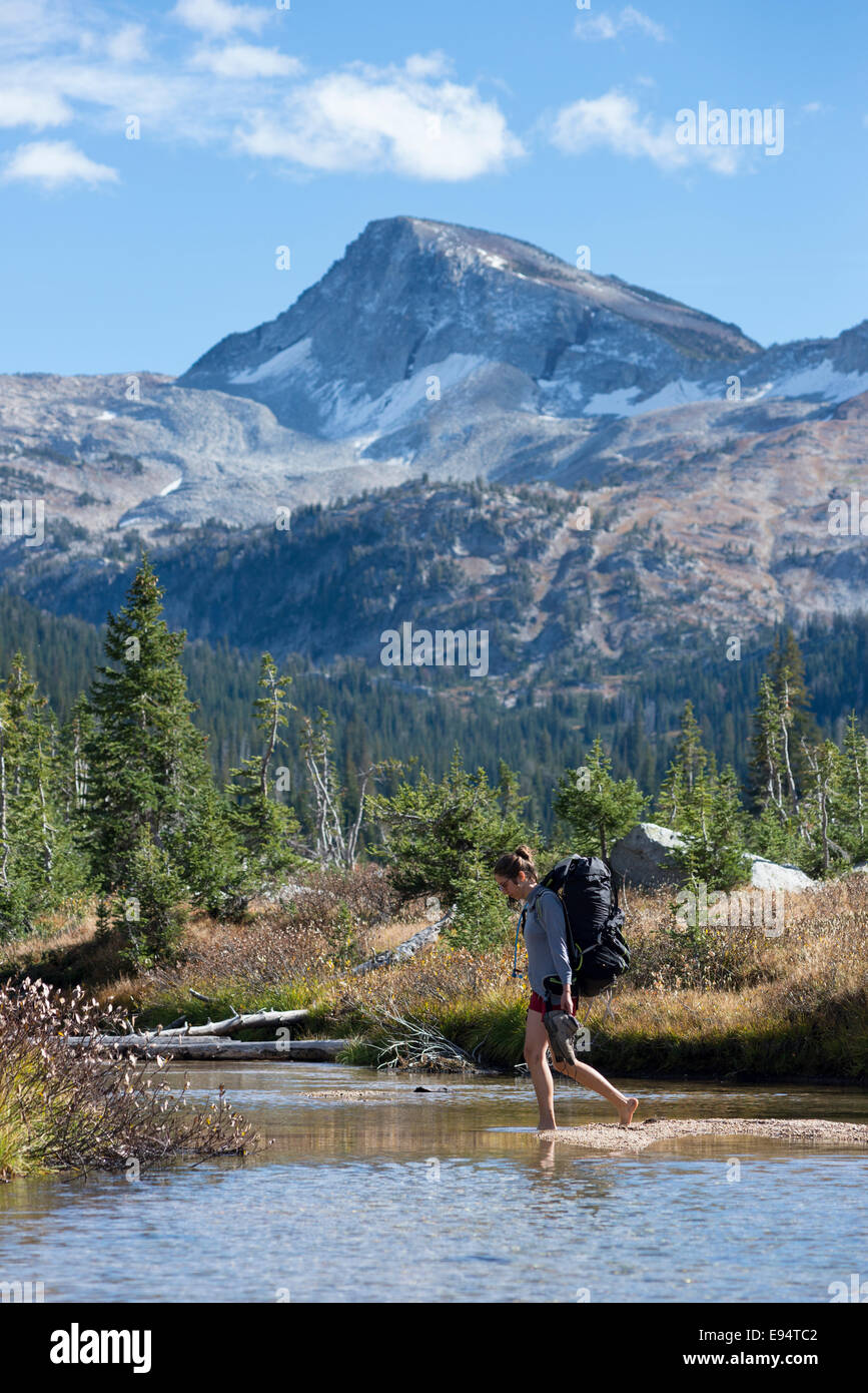 Femme traversant un ruisseau dans les montagnes de l'Oregon Wallowa. Cap de l'aigle pic est dans l'arrière-plan. Banque D'Images