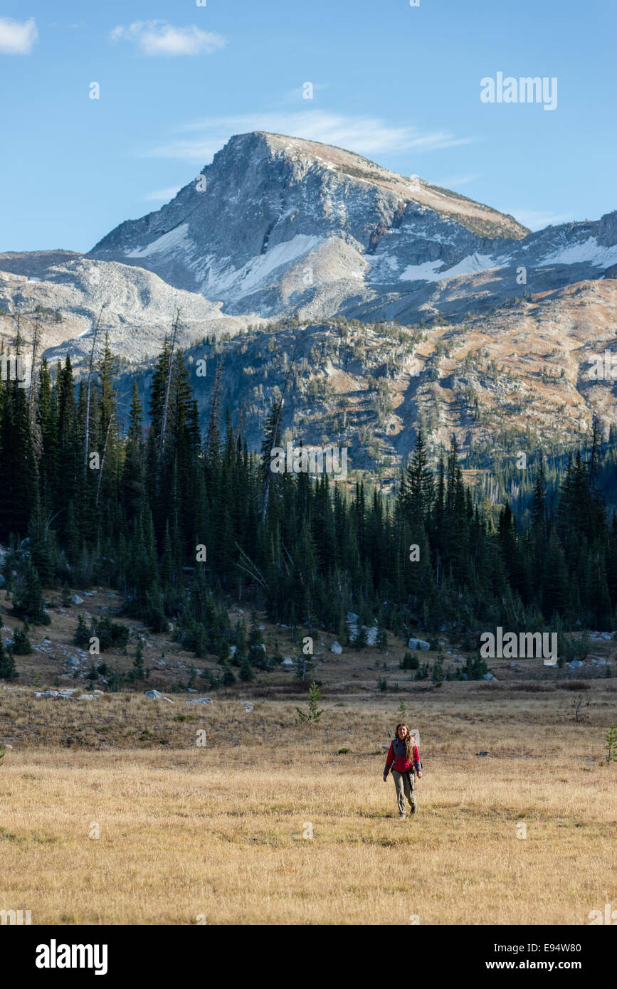 Femme de la randonnée à travers un pré sur un sac à dos voyage en Oregon's Montagnes Wallowa. Cap de l'aigle pic est dans l'arrière-plan. Banque D'Images