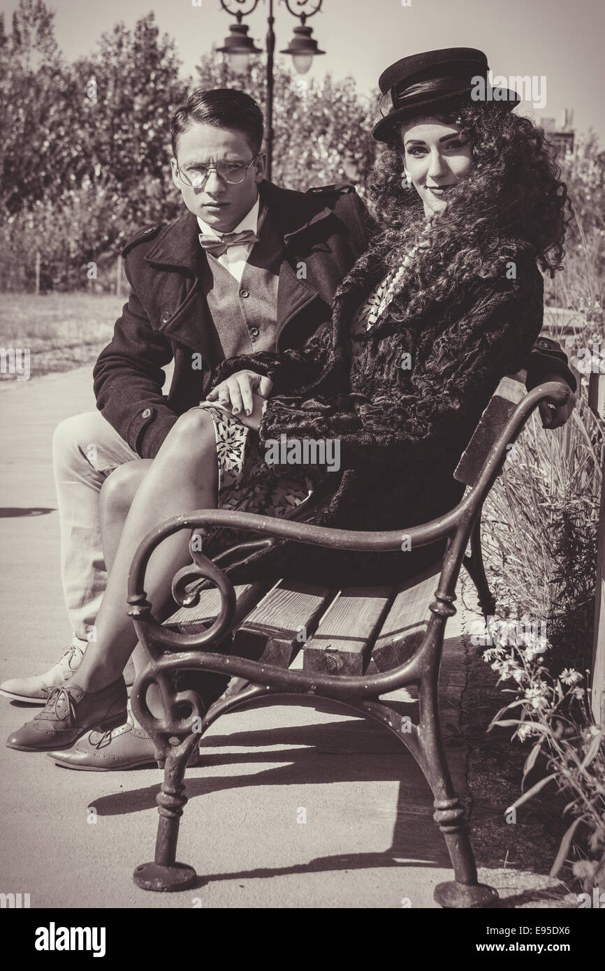 Fashion couple sitting on bench in vintage style et femme portant chapeau et manteau pour l'automne météo Banque D'Images