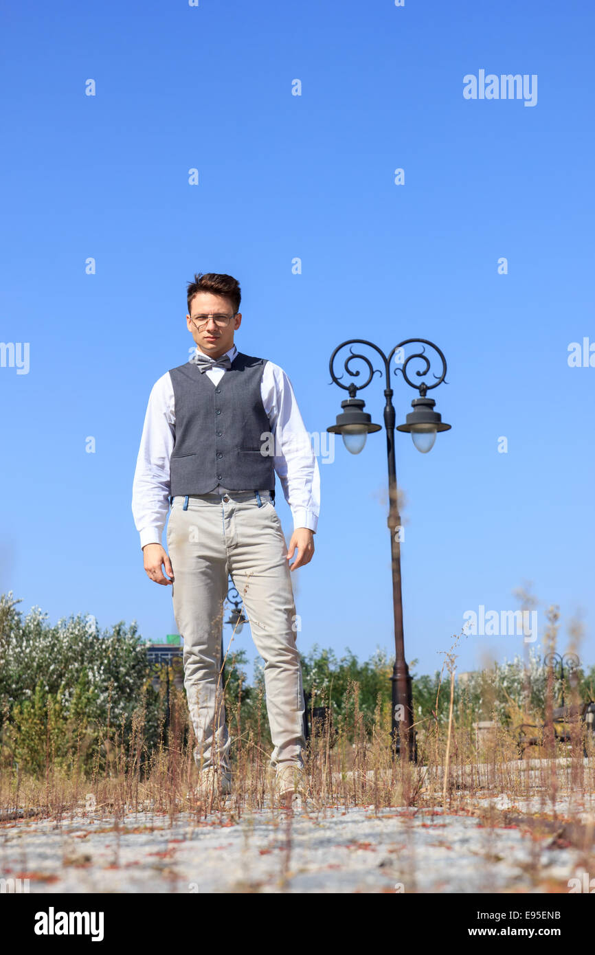 L'homme en chemise et gilet avec nœud papillon et des lunettes, debout dans des lignes de chemin de fer dans l'ancien vintage park et looking at camera Banque D'Images