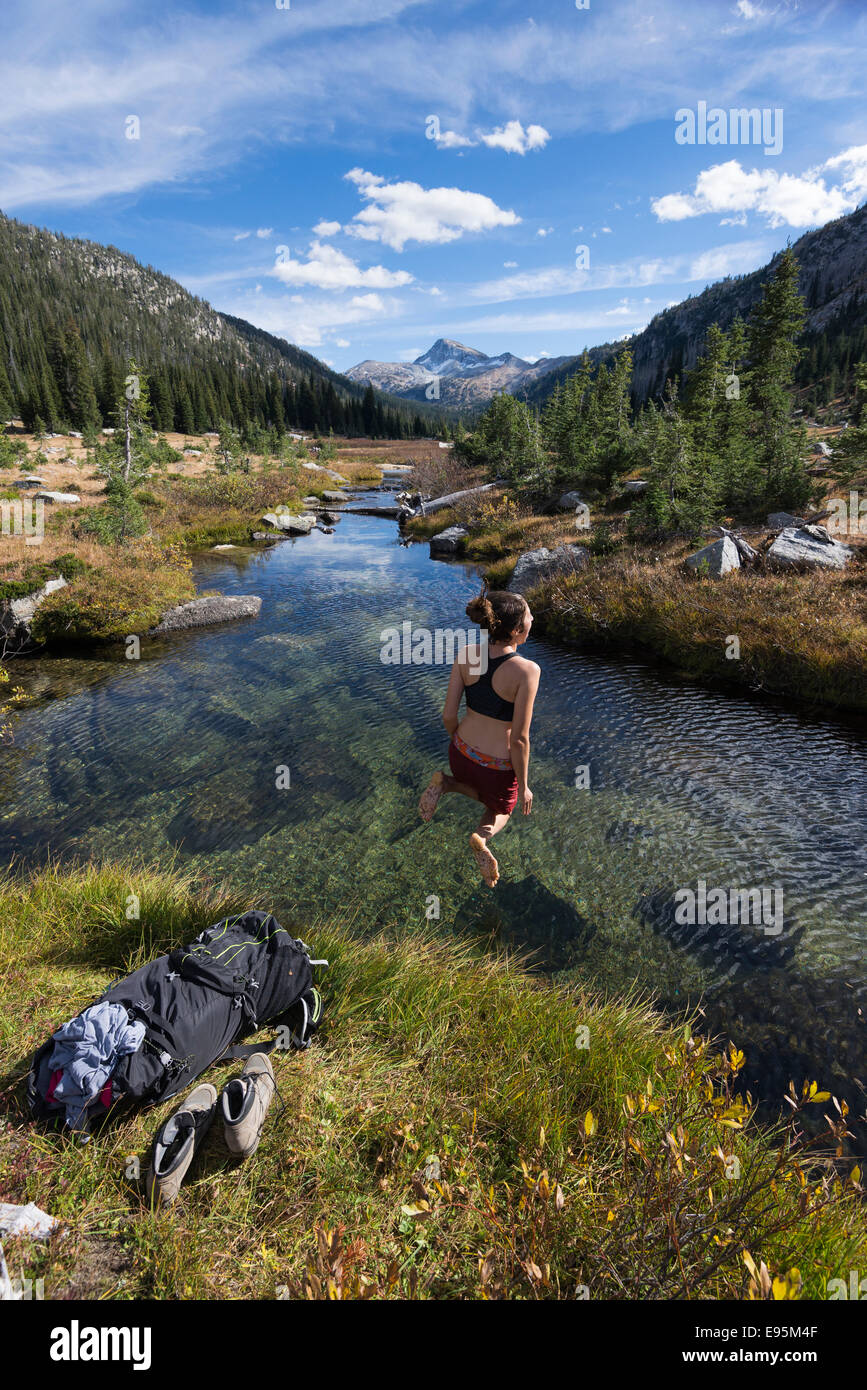 Femme sautant dans un ruisseau sur un sac à dos voyage en Oregon's Montagnes Wallowa. Banque D'Images