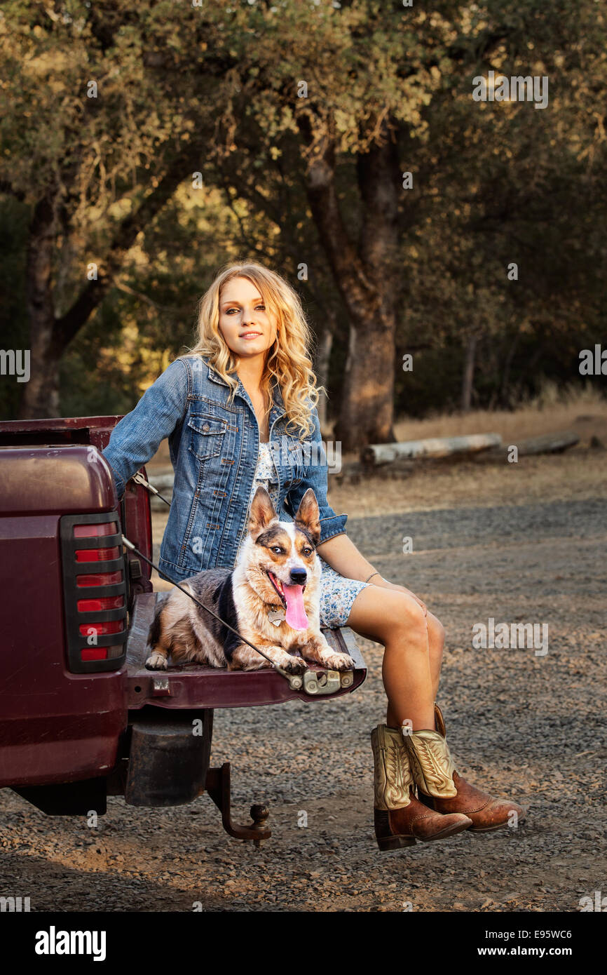 Une fille de la campagne et son chien détente sur une porte arrière ouverte à la fin d'une zone rurale, chemin de terre. Banque D'Images