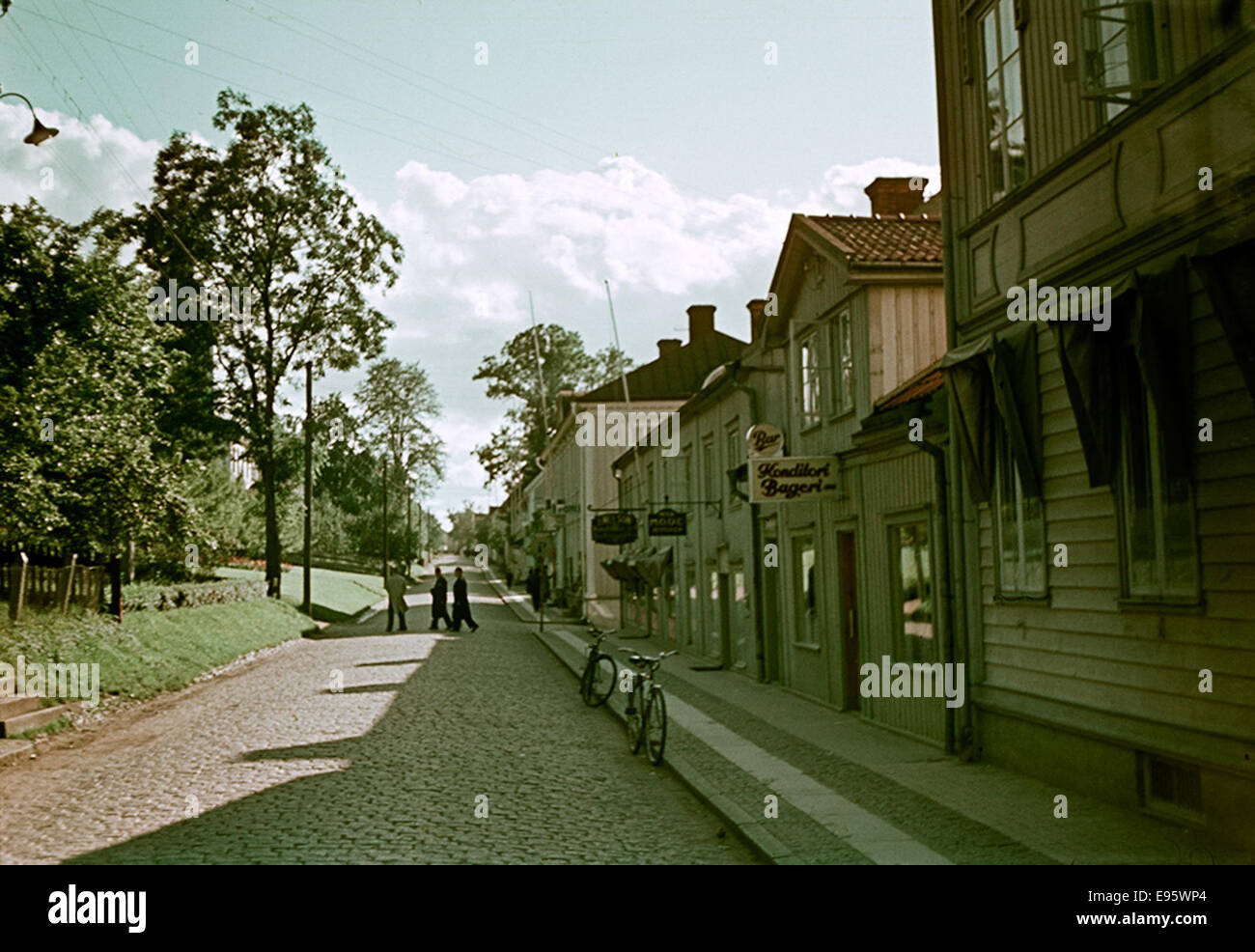 Cette photographie montre une scène de rue à Gränna, Småland, Suède, avec des vélos, des bâtiments, et des arbres visibles dans le cadre. Il a été pris par le Conseil du patrimoine national suédois et met en évidence une scène typique de village suédois de l'époque. Banque D'Images