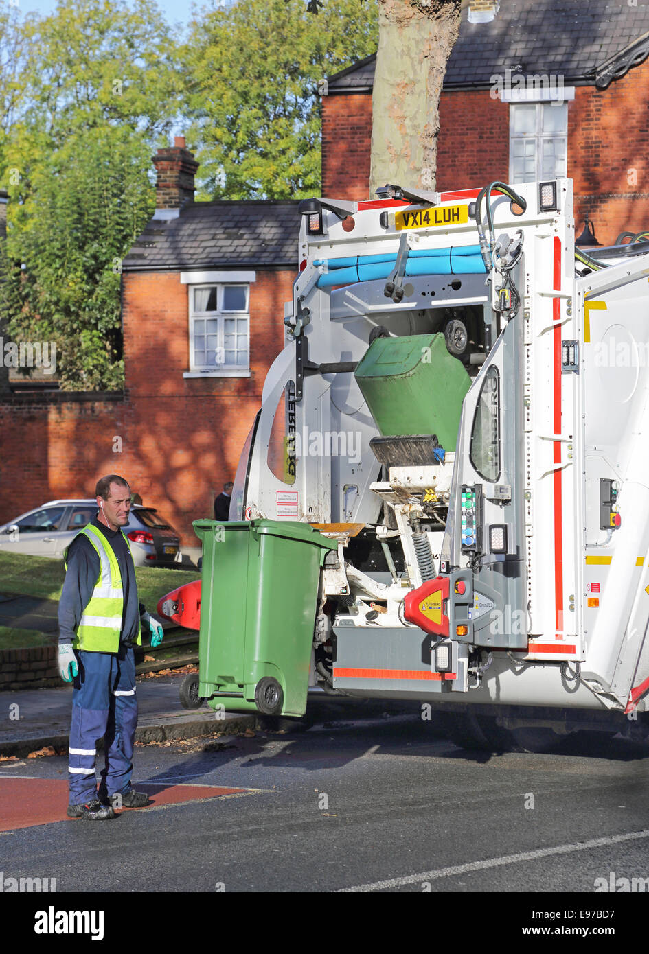 Un entrepreneur se jette une branche de refuser wheely bin dans un véhicule de collecte de déchets modernes Banque D'Images