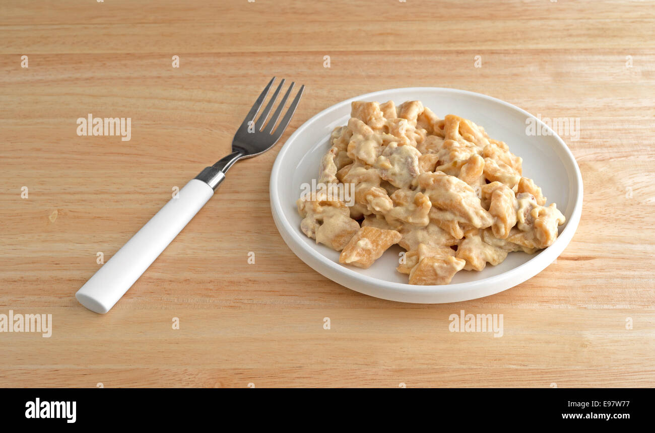 Une petite assiette de poulet sur les pâtes avec une sauce piment épais avec une fourchette pour le côté sur une table en bois et disponible Banque D'Images