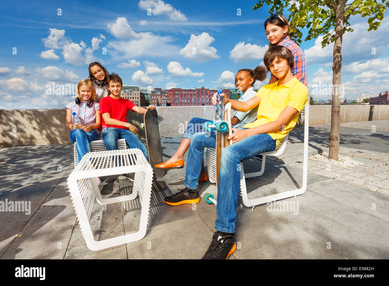 Les enfants positifs s'asseoir sur des chaises blanches avec des planches à roulettes Banque D'Images