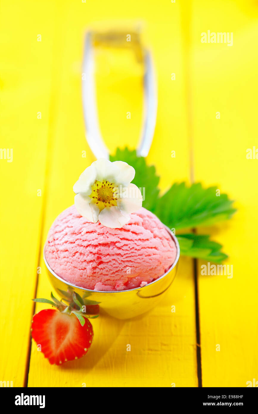 Pelle métallique rempli d'une boule de glace à la fraise garnie avec des fruits frais et une fleur peinte en jaune sur les planches de bois. Pour la glace concept Regardez mon portfolio Banque D'Images