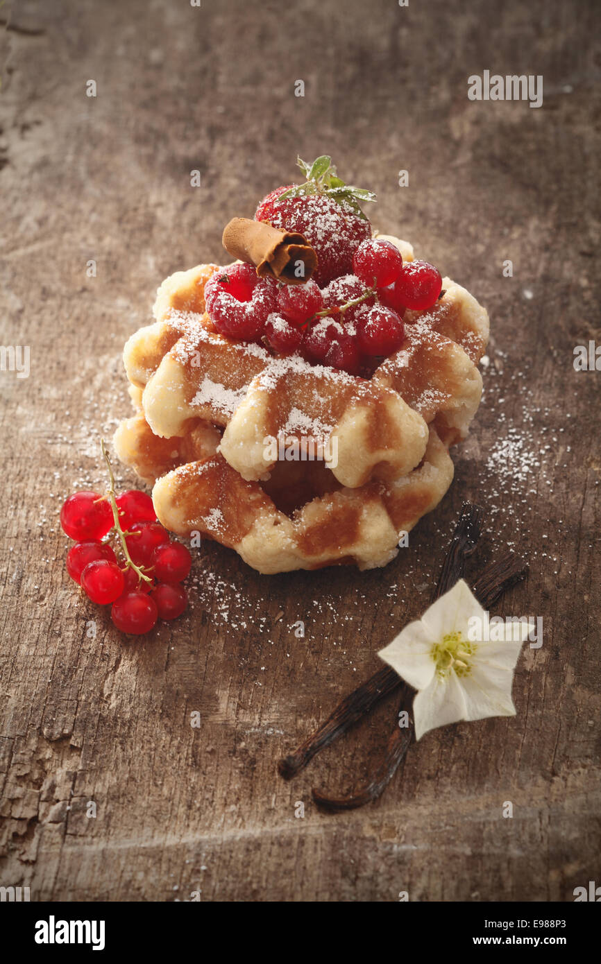 Gaufres garnies de framboises mûres, saupoudrés de sucre sur une table en bois rustique avec des gousses de vanille et de groseilles Banque D'Images