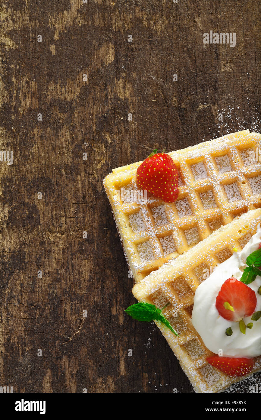 Vue aérienne de gaufres d'or avec de la crème et des fraises sur une table en bois texturé avec copyspace Banque D'Images