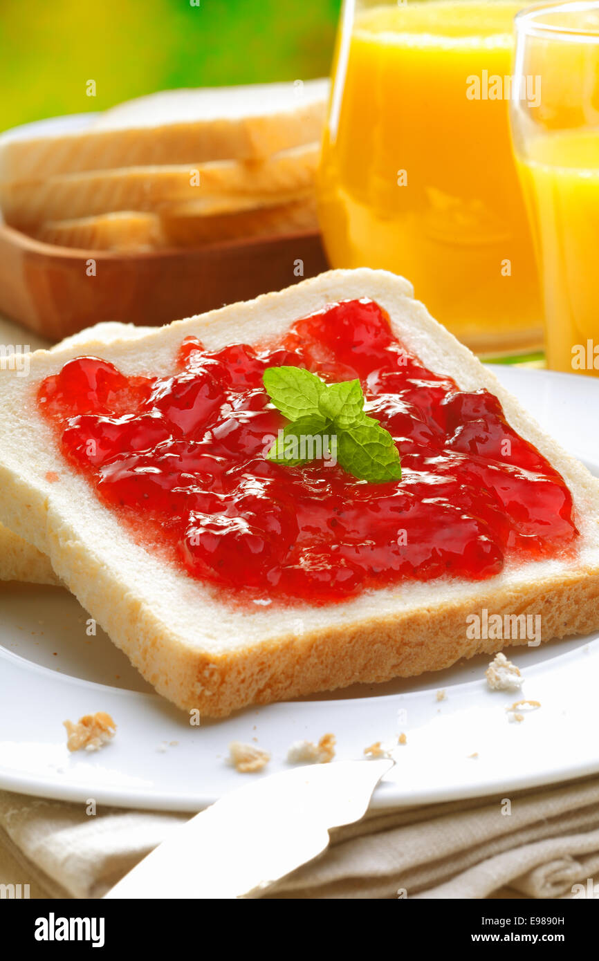 Dynamique de couleur Red Strawberry Topping préserver une tranche de pain blanc frais sur une assiette de chapelure servi avec du jus d'orange pour le petit déjeuner Banque D'Images