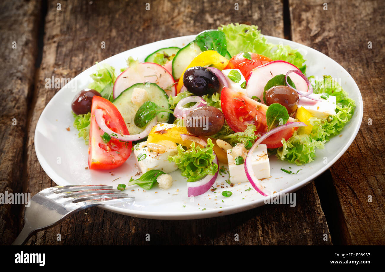 Servant de frais sain salade mélangée avec des légumes verts, radis, tomate, olives et fromage servi sur une table en bois rustique Banque D'Images