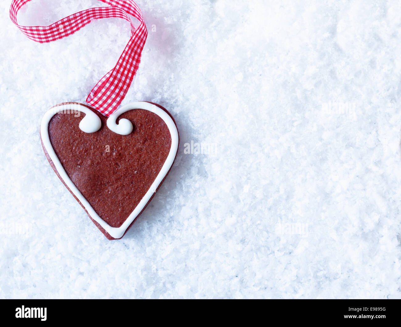 Coeur d'épices avec glaçage décoratif et festif d'un ruban à carreaux rouge et blanc sur la neige avec copyspace pour Noël ou votre Valentine bonjour Banque D'Images