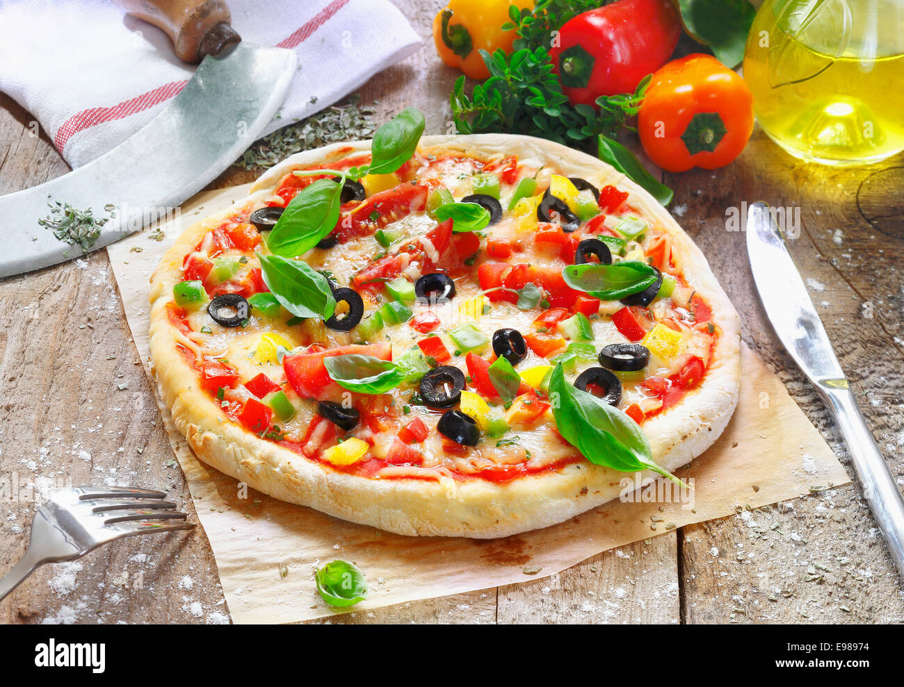 Pizza végétarienne fraîchement préparé servi sur du papier four dans la cuisine, entouré de divers ingrédients utilisés dans la préparation Banque D'Images