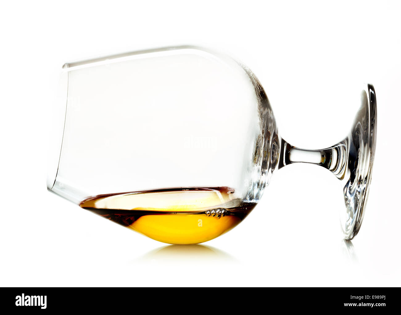 Or brillant cognac ou brandy dans un petit verre verre allongé sur le côté, sur un fond blanc Banque D'Images