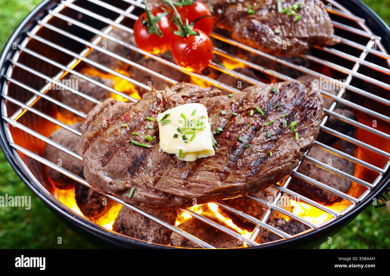 Portrait d'une partie du lean steak garni de beurre et fines herbes griller sur un feu dans un barbecue portable à l'extérieur sur l'herbe Banque D'Images