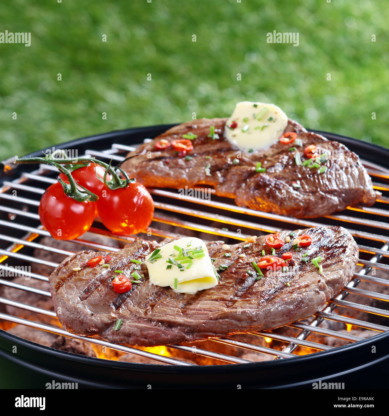 Partie de délicieux steak maigre surmonté avec le beurre et les herbes grillées sur un barbecue sur rouge les tisons en plein air sur la pelouse Banque D'Images