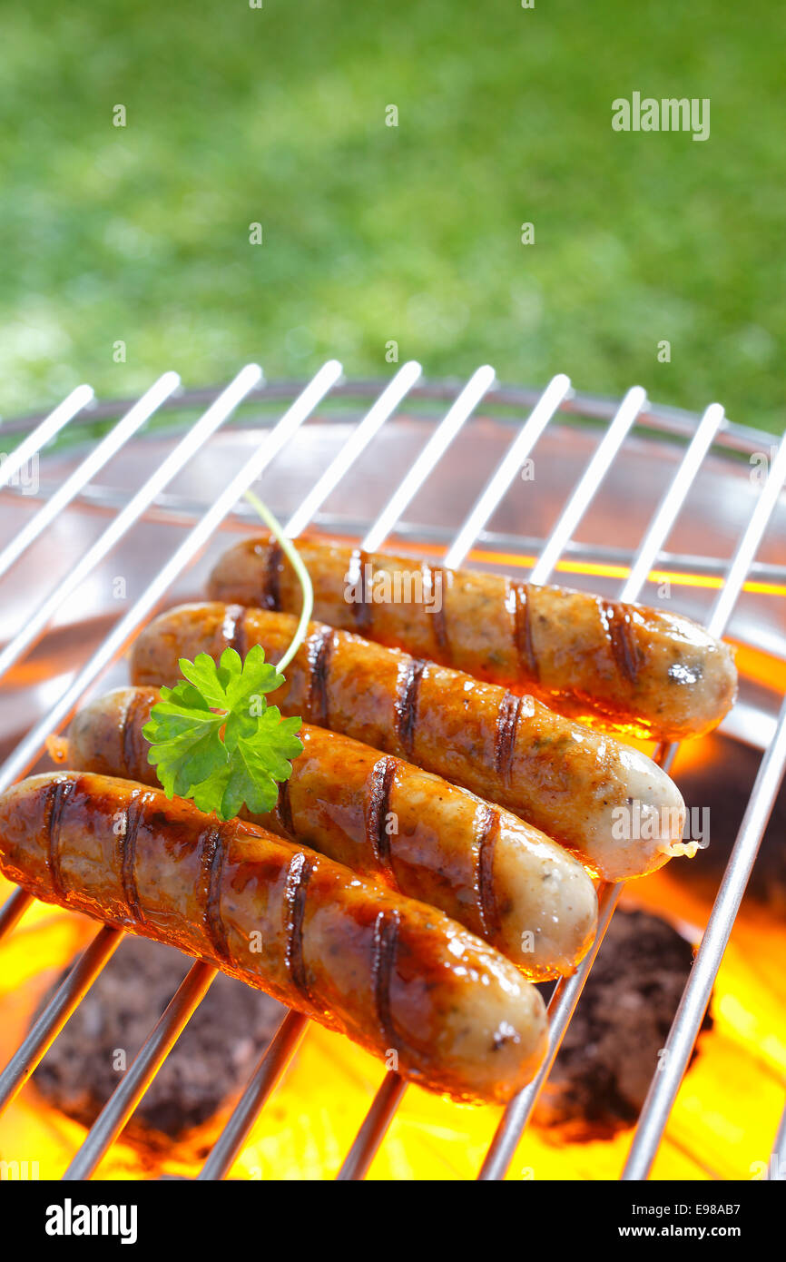 De délicieuses saucisses grillées en appui sur le fer à repasser grille d'un barbecue portable plus de braise qu'ils cuisinent à la perfection Banque D'Images