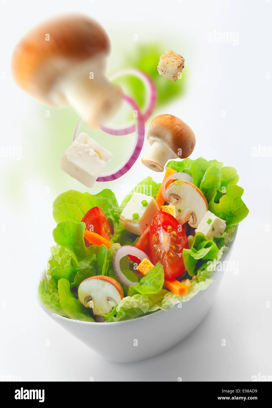 Portrait d'un bol de mélange frais et sain salade de laitue, tomates, fromage, oignons et champignons tranchés sur un fond blanc avec des ingrédients floue Banque D'Images