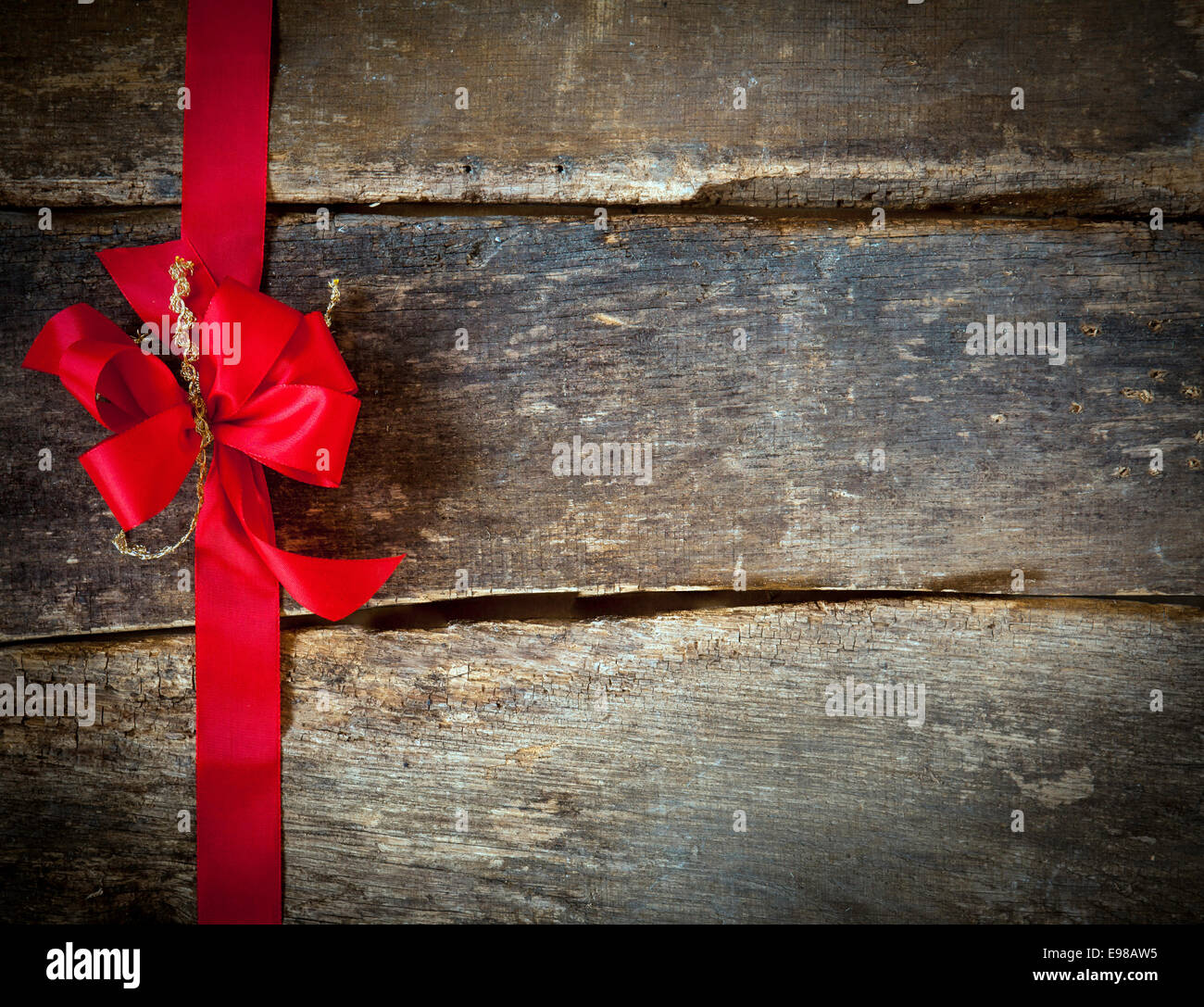 Arc rouge festif et ruban formant une frontière pour une carte de Noël sur planches en bois rustique avec copyspace pour votre message d'accueil ou qu'il souhaite Banque D'Images