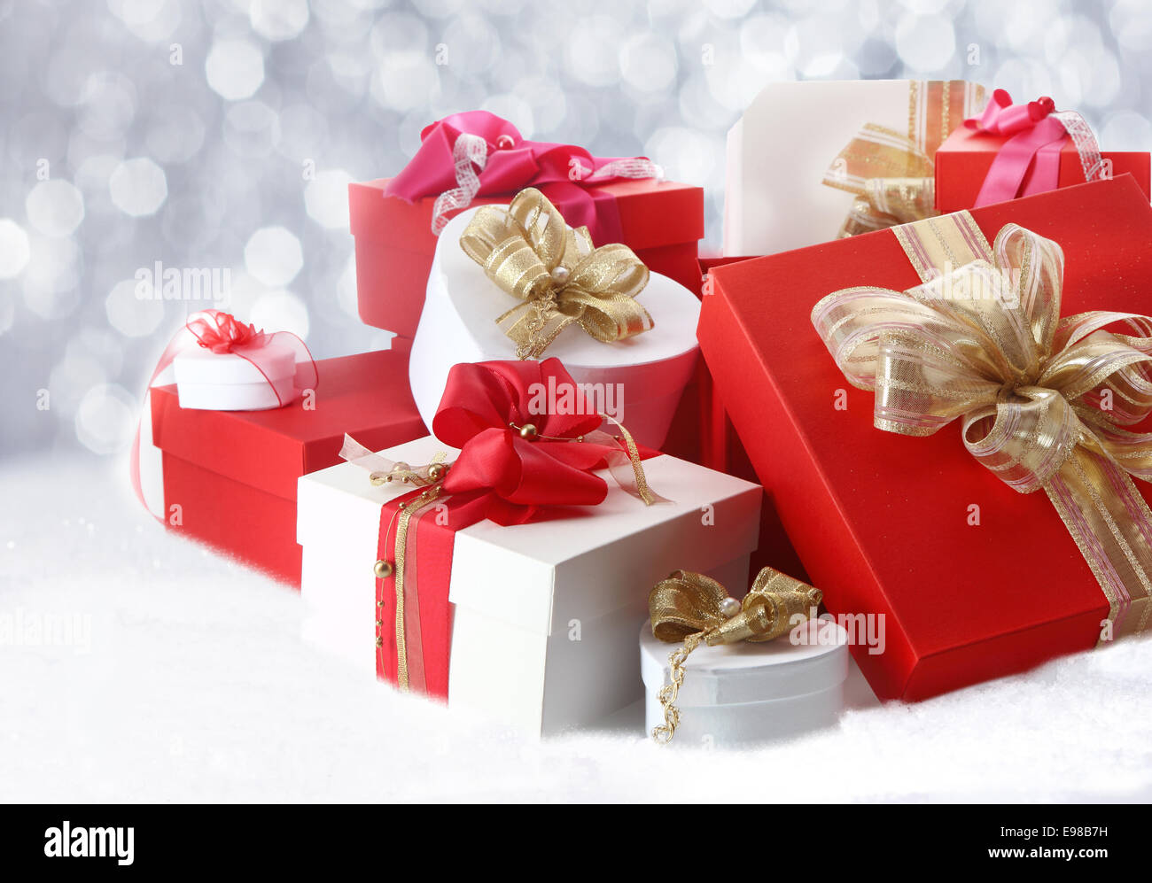 Jolie cadeaux de Noël et des boîtes avec des arcs et des rubans en rouge, blanc et or, sur un lit de neige blanc hiver Banque D'Images