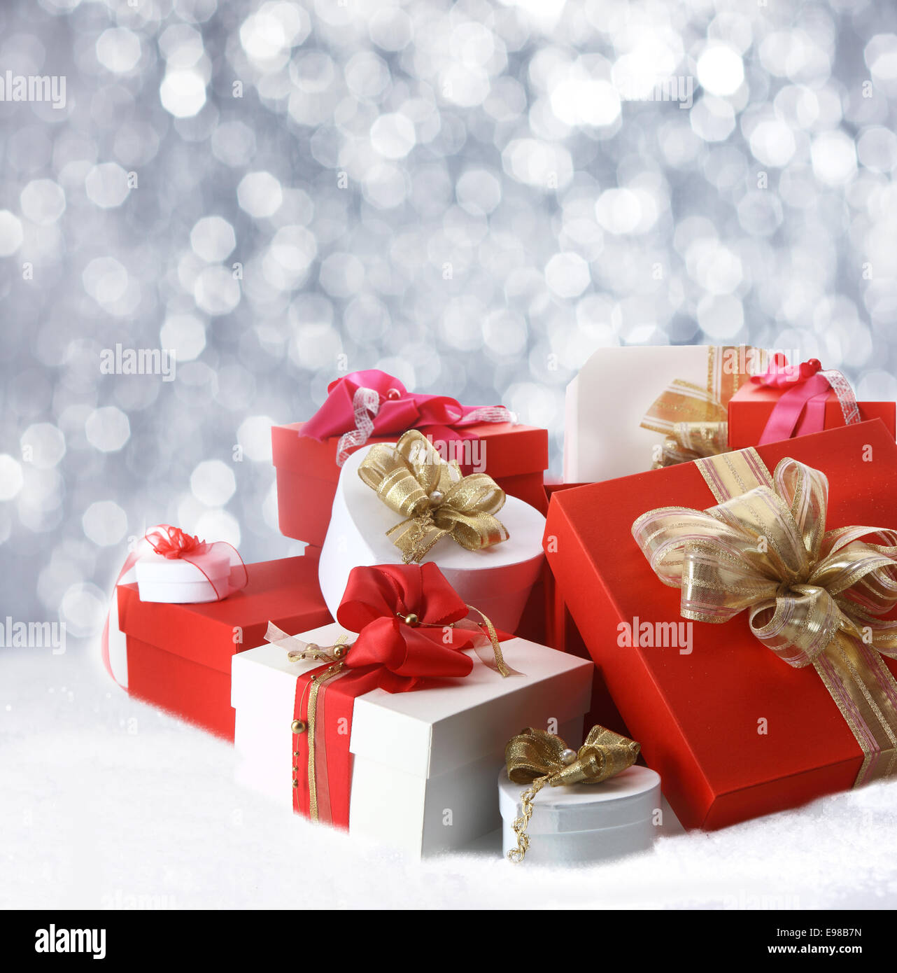 Collection de cadeaux de Noël décoration de fête en rouge, blanc et or couché dans la neige d'hiver contre un bokeh de parti mousseux Banque D'Images