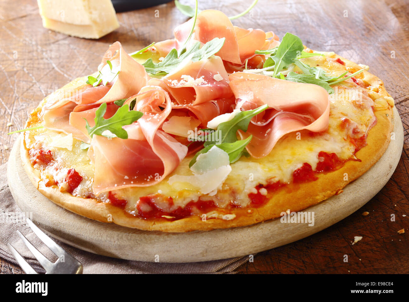 Pizza prosciutto italien avec du jambon et des feuilles de roquette sur une base de fromage et la pâte de tomate servi sur un sol en bois rustique Banque D'Images