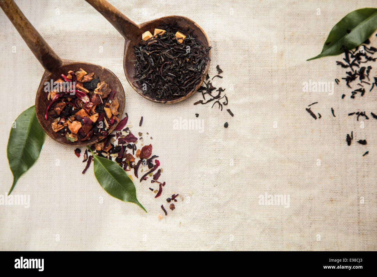 Des feuilles séchées du thé dans deux petites cuillères en bois avec plateau traditionnel et un mélange plus exotiques de thé séchées, des herbes et des fruits pour une bonne boisson savoureuse sur un fond textile texturé avec copyspace Banque D'Images